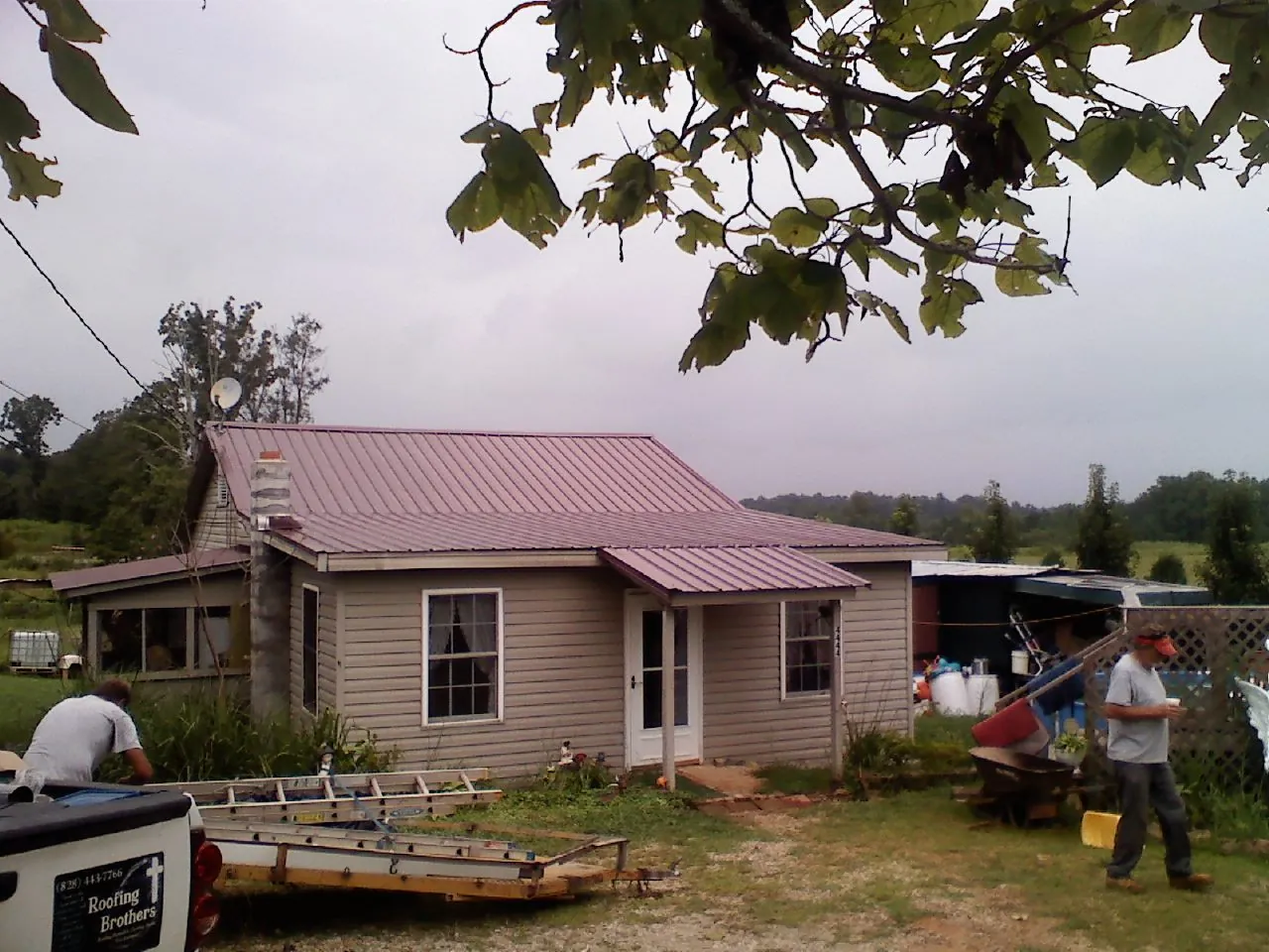 Crew finishing a mauve metal roof on a small farmhouse in Seneca
